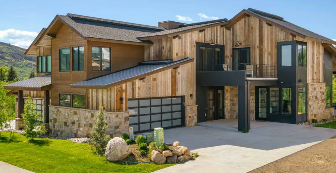 Exterior of a modern home with stone and timber cladding, a landscaped lawn and a boulder garden
